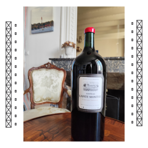 Une bouteille Impériale (6 litres) de vin rouge Bordeaux Supérieur du Château Lafite Monteil, posée sur une table en bois devant une cheminée