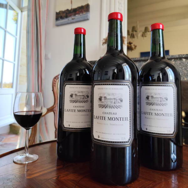 Trois double magnum de vin rouge du Château Lafite Monteil posées sur une table, avec un verre de vin devant une cheminée