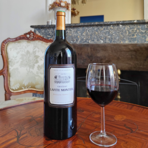 Un magnum de vin rouge du Château Lafite Monteil posé sur une table en bois devant une cheminée, avec un verre de vin rouge