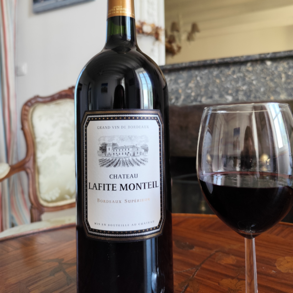 Un magnum de vin rouge du Château Lafite Monteil posé sur une table en bois devant une cheminée, avec un verre de vin rouge